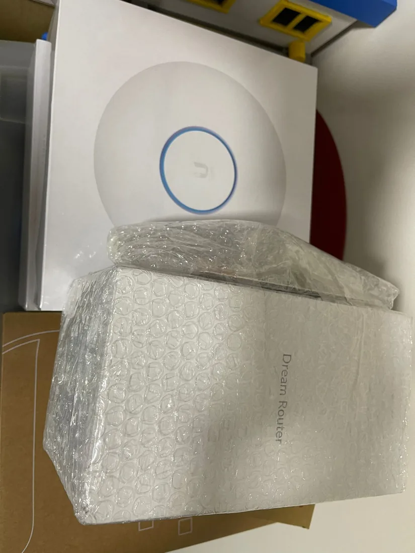 A boxed Ubiquiti UniFi ceiling access point and a bubble-wrapped UniFi Dream Router.