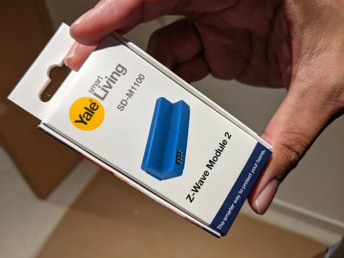 A Yale Smart Living SD-M1100 Z-Wave Module 2 in its retail packaging, held in one hand.