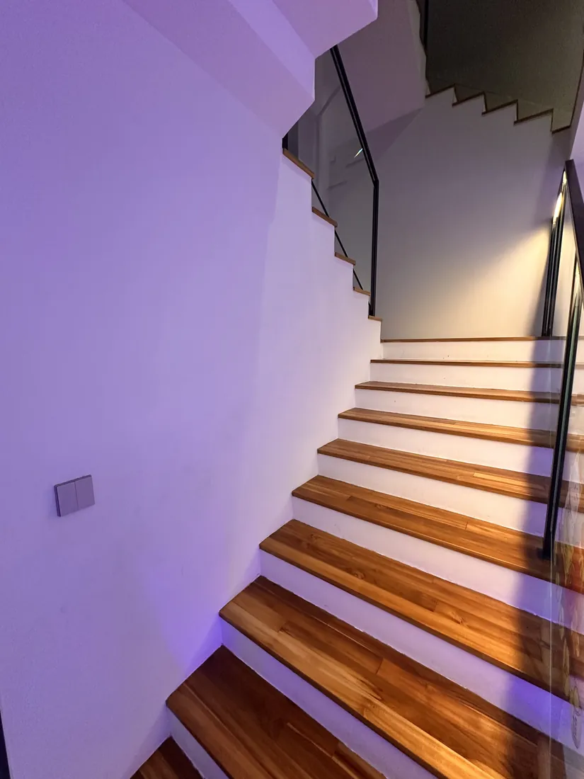 Staircase at Cedar Avenue with timber treads lit warm and the adjacent wall washed in lilac