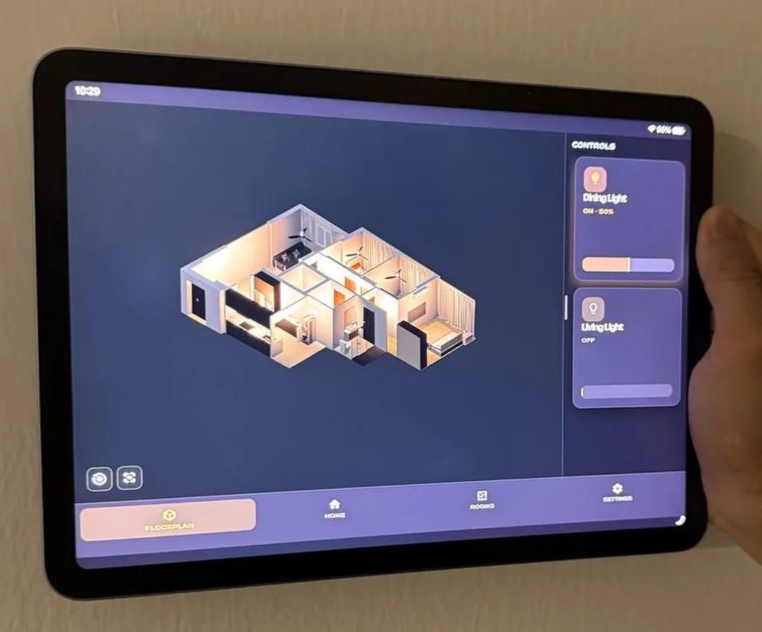 A wall-mounted tablet showing an isometric 3D floorplan of a flat, with a controls panel dimming the dining light to 50 percent and the living light switched off.