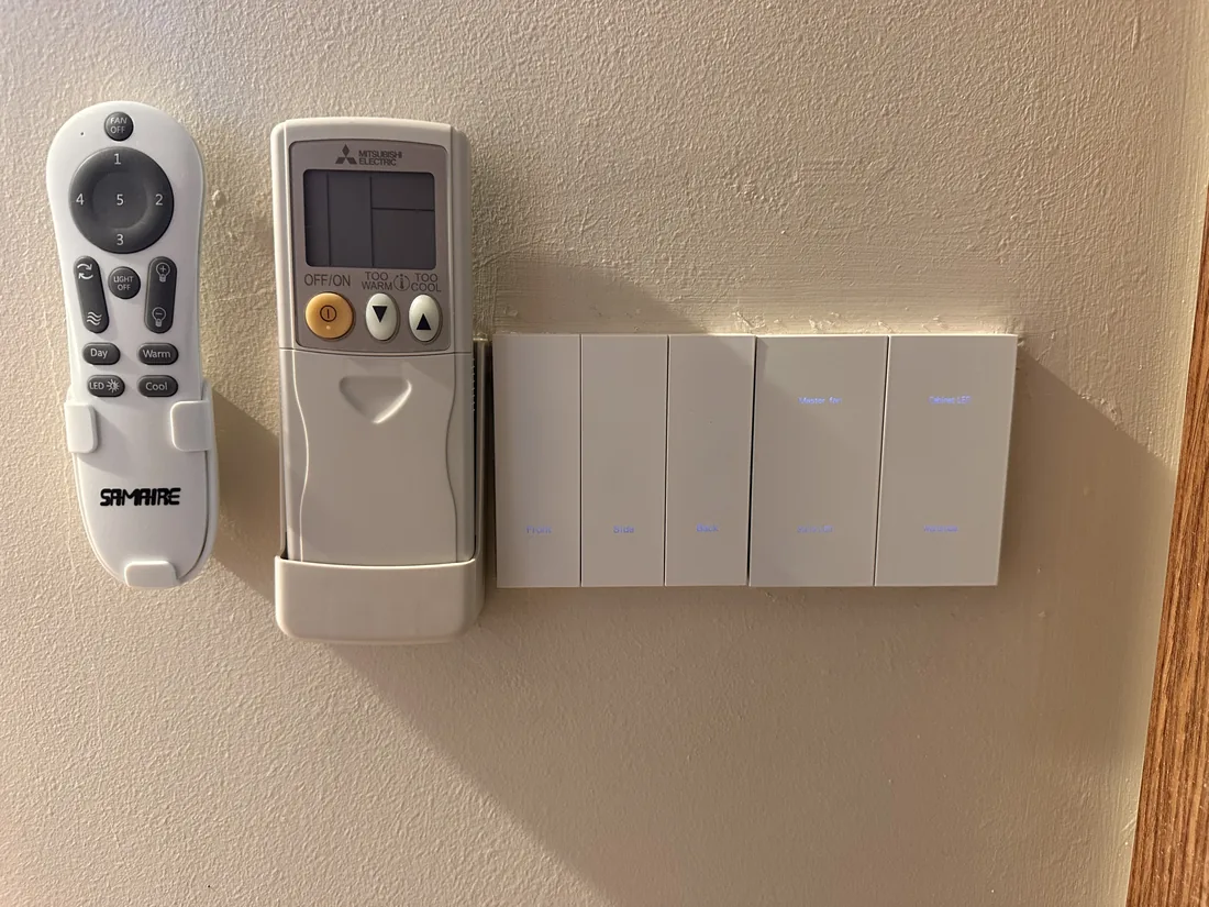 A ceiling fan remote and an air-conditioner remote in wall holders beside conventional switch plates.