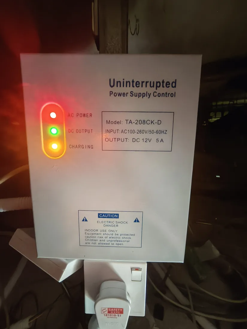 A wall-mounted uninterruptible power supply control panel with power, output and charging status lights lit.