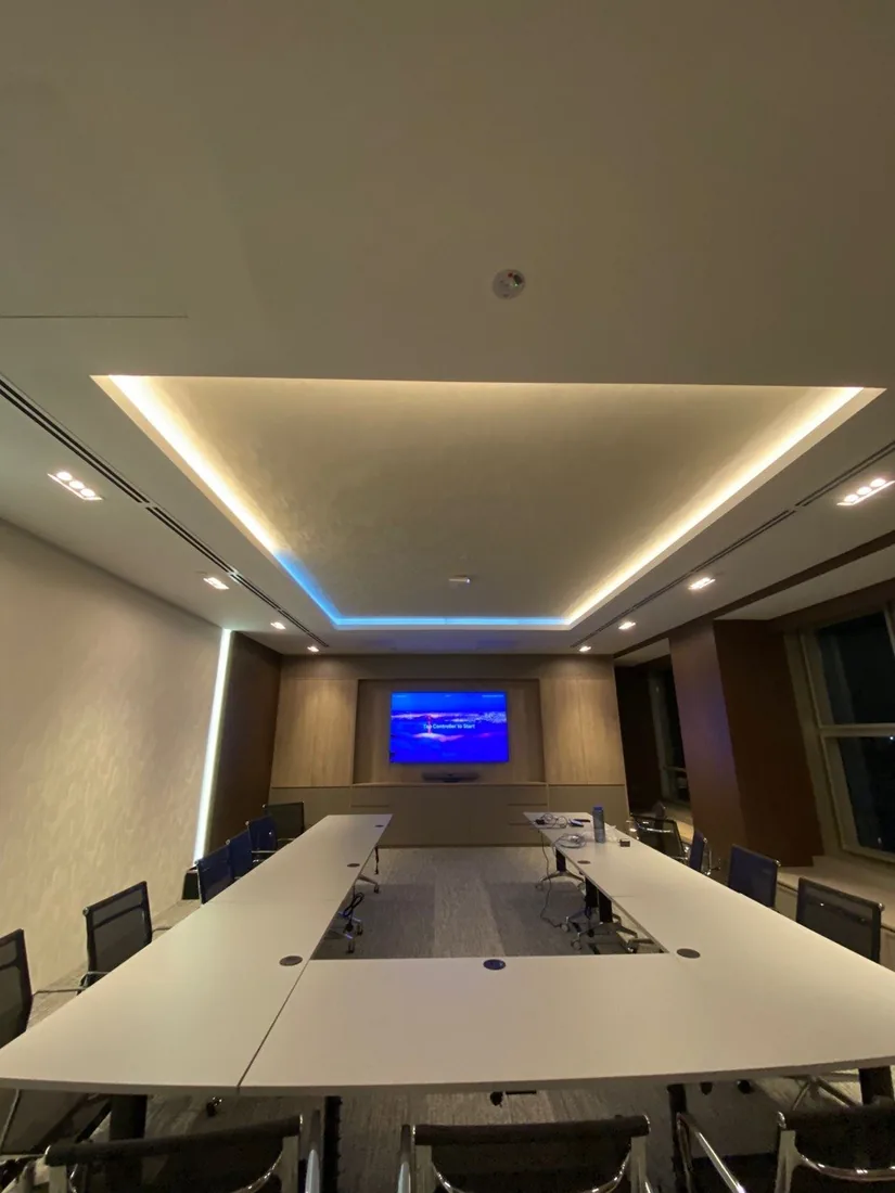A meeting room with a long table, concealed cove lighting and a wall-mounted display.