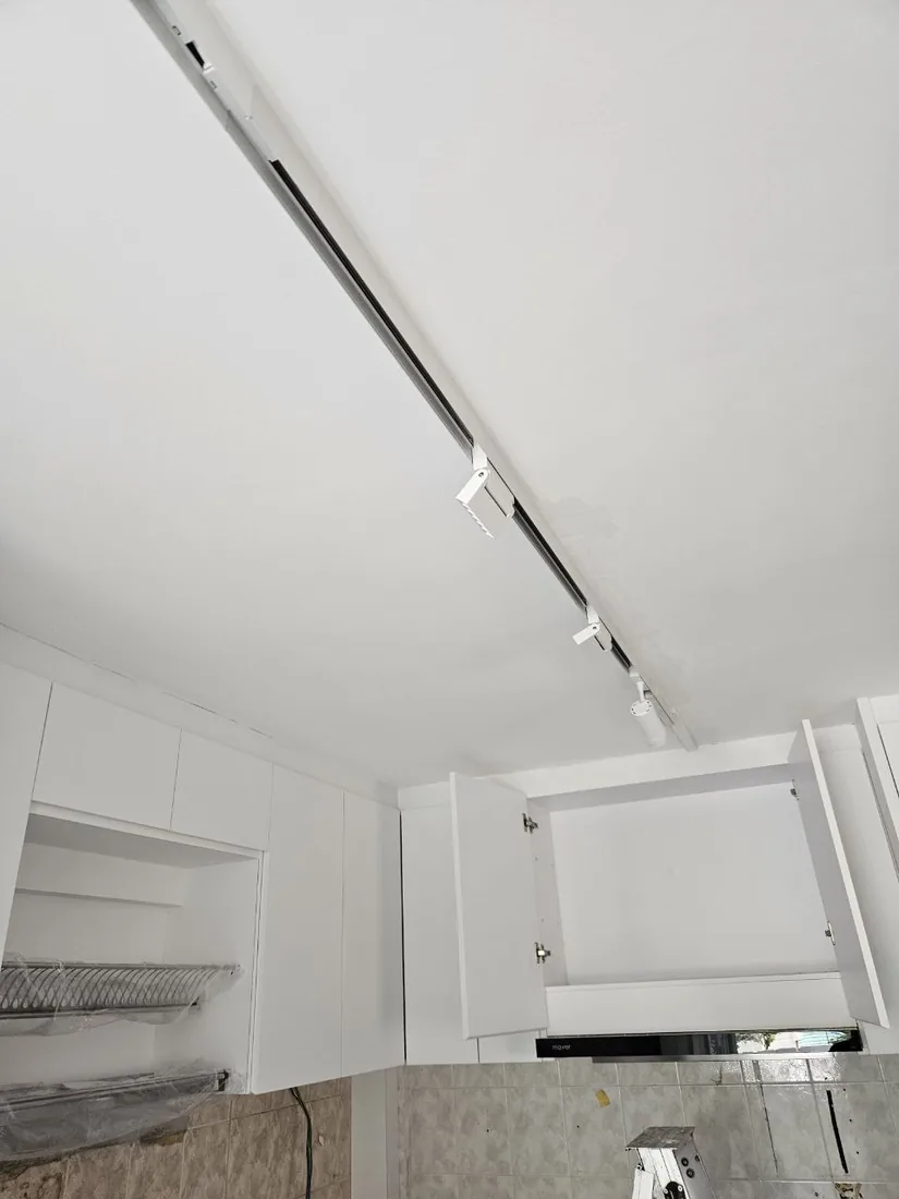 A slim track-lighting run mounted along a ceiling above fitted cabinetry.