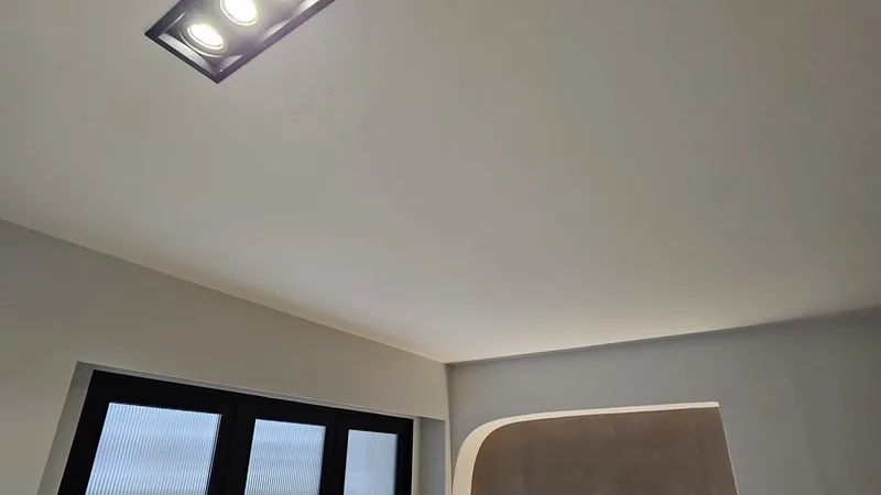 A recessed multi-head downlight and a warm cove-lit niche beside a full-height window.