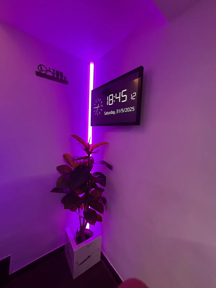 A vertical LED strip lighting a corner in magenta, next to a wall-mounted clock display.