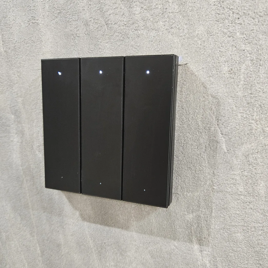 A three-gang smart switch panel on a wall, each gang showing a small status indicator.