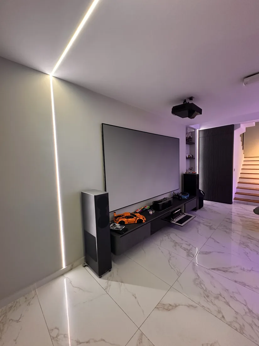 A home theatre with a projection screen, floor-standing speakers and concealed cove lighting.