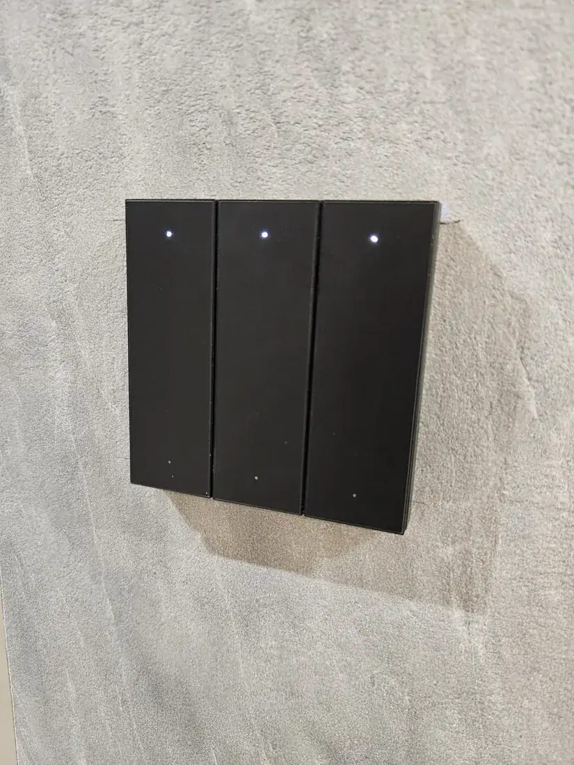 Black three-gang smart switch mounted on a concrete-effect wall at Woodlands